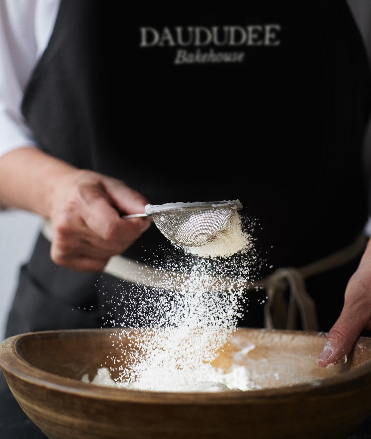 Daududee Bakehouse baker sifting flour into a wooden bowl